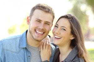 Front view of a couple posing outdoors with perfect smile and white teeth and looking at you in a park