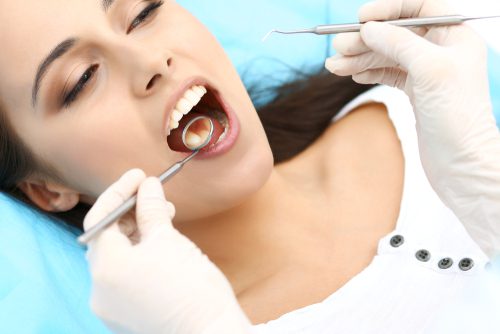 beautiful woman with healthy straight white teeth sitting at dental chair with open mouth during oral checkup while doctor working at teeth-img-blog