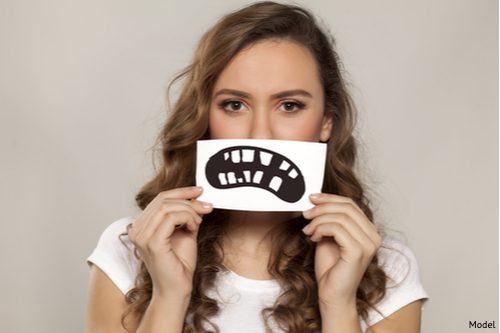 Brunette woman on grey background holding up a cartoon mouth representing tooth decay.