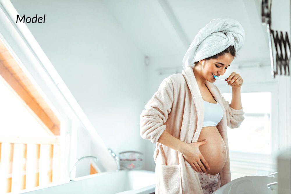 Woman brushing her teeth while pregnant to protect the health of her baby.